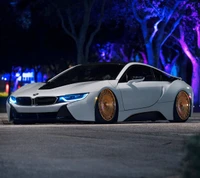 Elegante BMW i8 blanco con llamativas ruedas doradas bajo una iluminación etérea