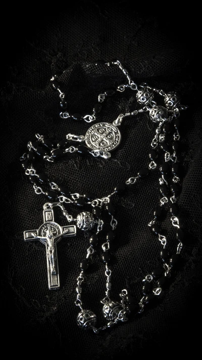 Silver chain rosary with a cross and round beads on a dark background.