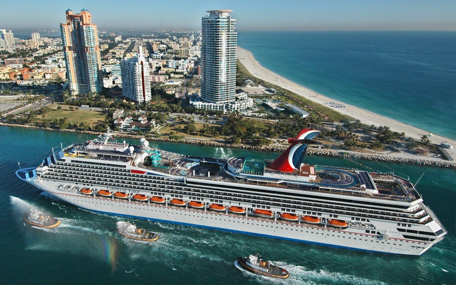 Ein kreuzfahrtschiff im wasser mit einer stadt im hintergrund. (carnival cruise line, kreuzfahrtschiff, schiff, wassertransport, passagierschiff)