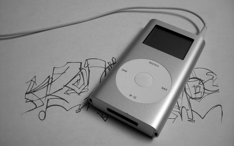 Близкий план ipod, лежащего на столе с рисунком человека (портативный медиаплеер, айпод, ipod, электронное устройство, дизайн)