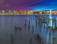 Horizonte de la ciudad de Nueva York por la noche con exposición prolongada y reflejos en el muelle