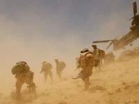 Soldiers navigating a dusty landscape in Afghanistan as a Boeing CH-47 Chinook hovers nearby.