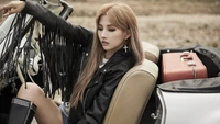 Soyeon from (G)I-DLE posing stylishly in a vintage car, showcasing a bold fashion statement with a leather jacket and striking accessories.