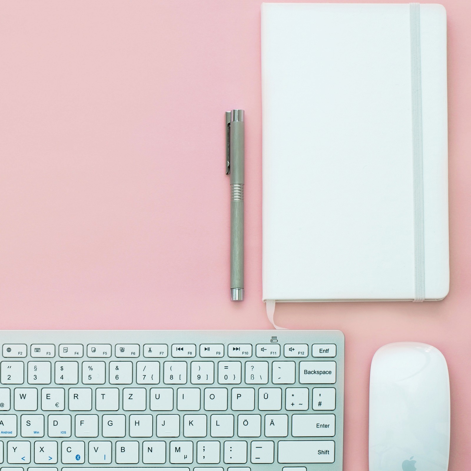 Hay un teclado, un ratón y un cuaderno sobre una superficie rosa (atrás, elegante, familia, teclado, vida)