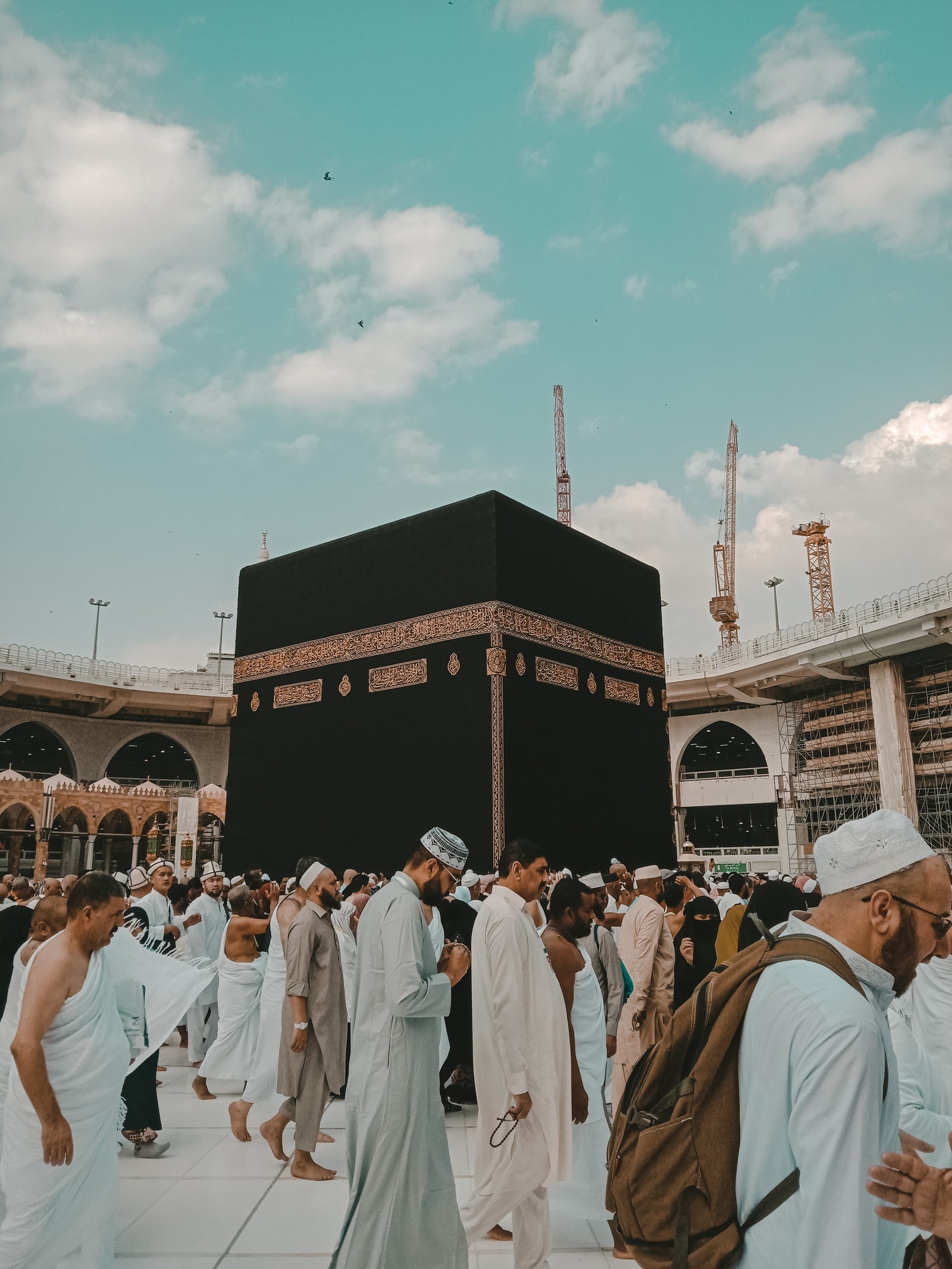 Menschen stehen um einen schwarzen würfel in einem großen gebäude (islam, islamisch, kaba, kabba, saudi arabien)