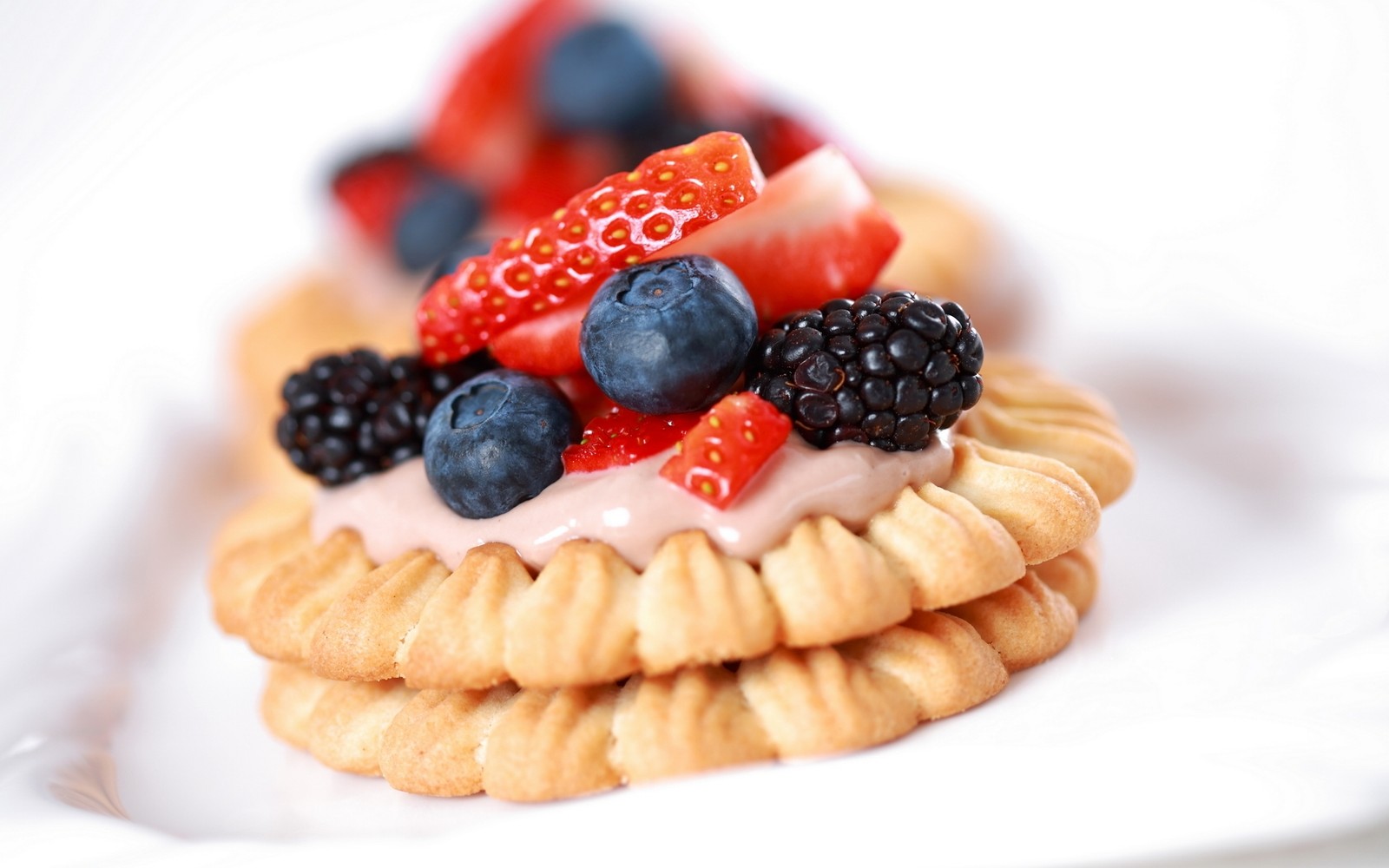 Es gibt ein kleines dessert mit beeren und sahne auf einem teller (essen, süße, gefrorenes dessert, keks, frucht)