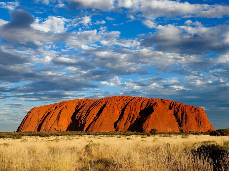 Крупный план большого камня посреди поля (улуру, uluru, скала, бедлендс, облако)