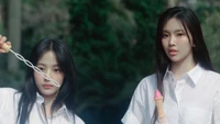 Les membres de NewJeans Minji et Hyein jouent avec du chewing-gum dans un cadre extérieur luxuriant.