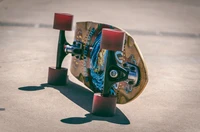 Bunter Longboard, der auf einer Betonoberfläche ruht und sein kompliziertes Design sowie die lebhaften Räder zeigt.