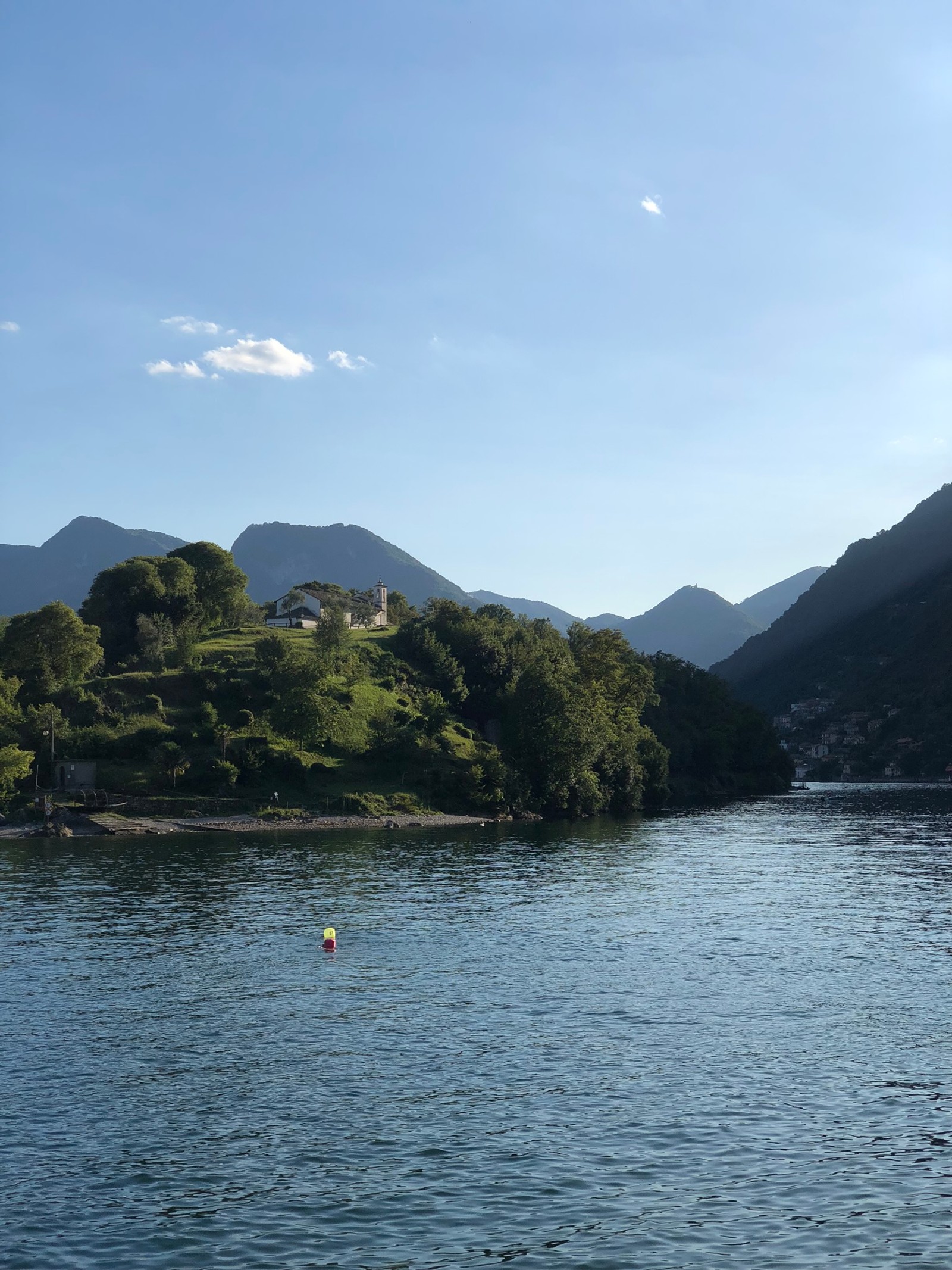 Há um pequeno barco flutuando na água (lago, corpo de água, formas montanhosas, natureza, vegetação)