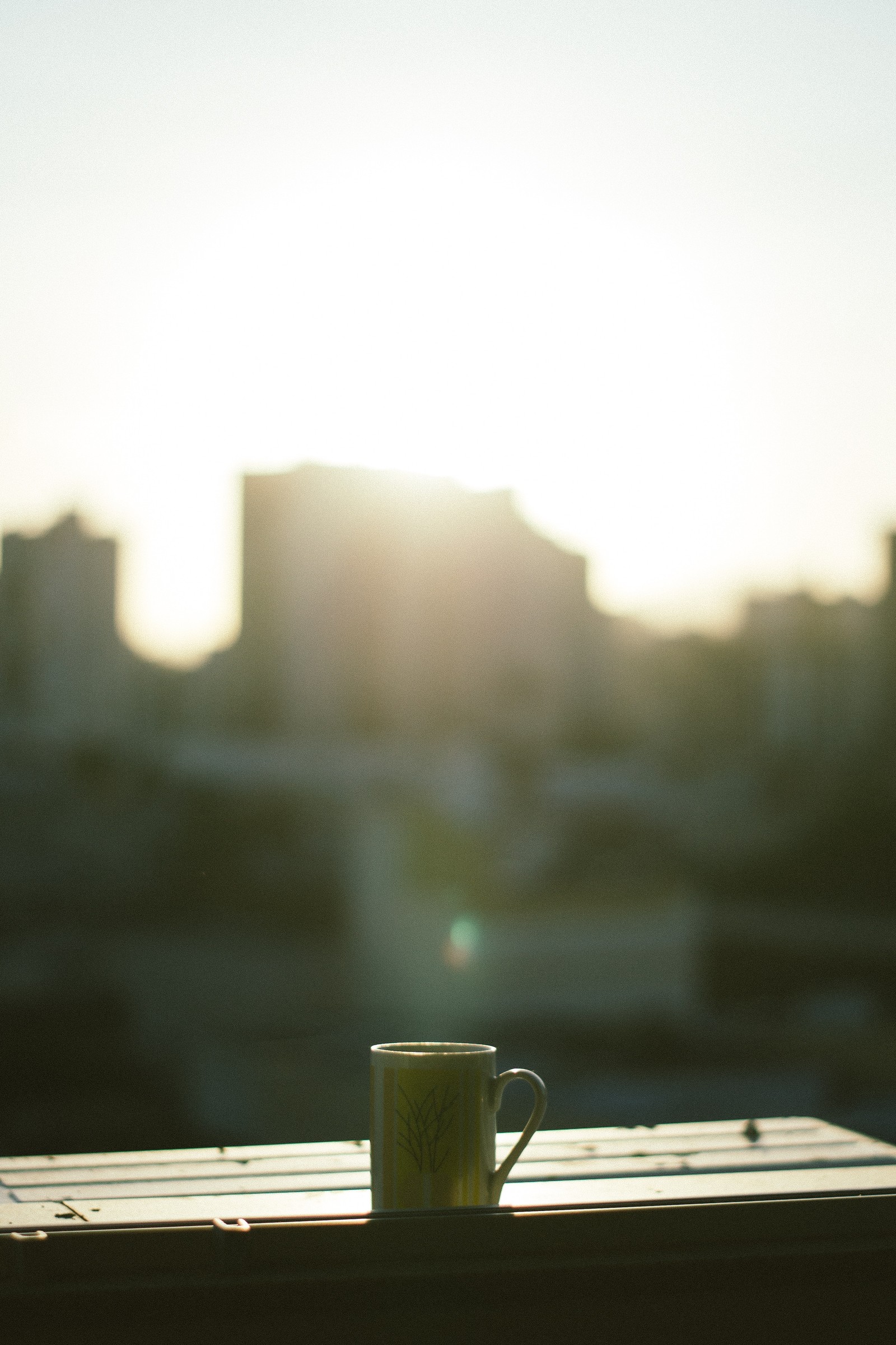 There is a cup of coffee sitting on a table with the sun setting in the background (light, sunlight, morning, cloud, atmosphere)