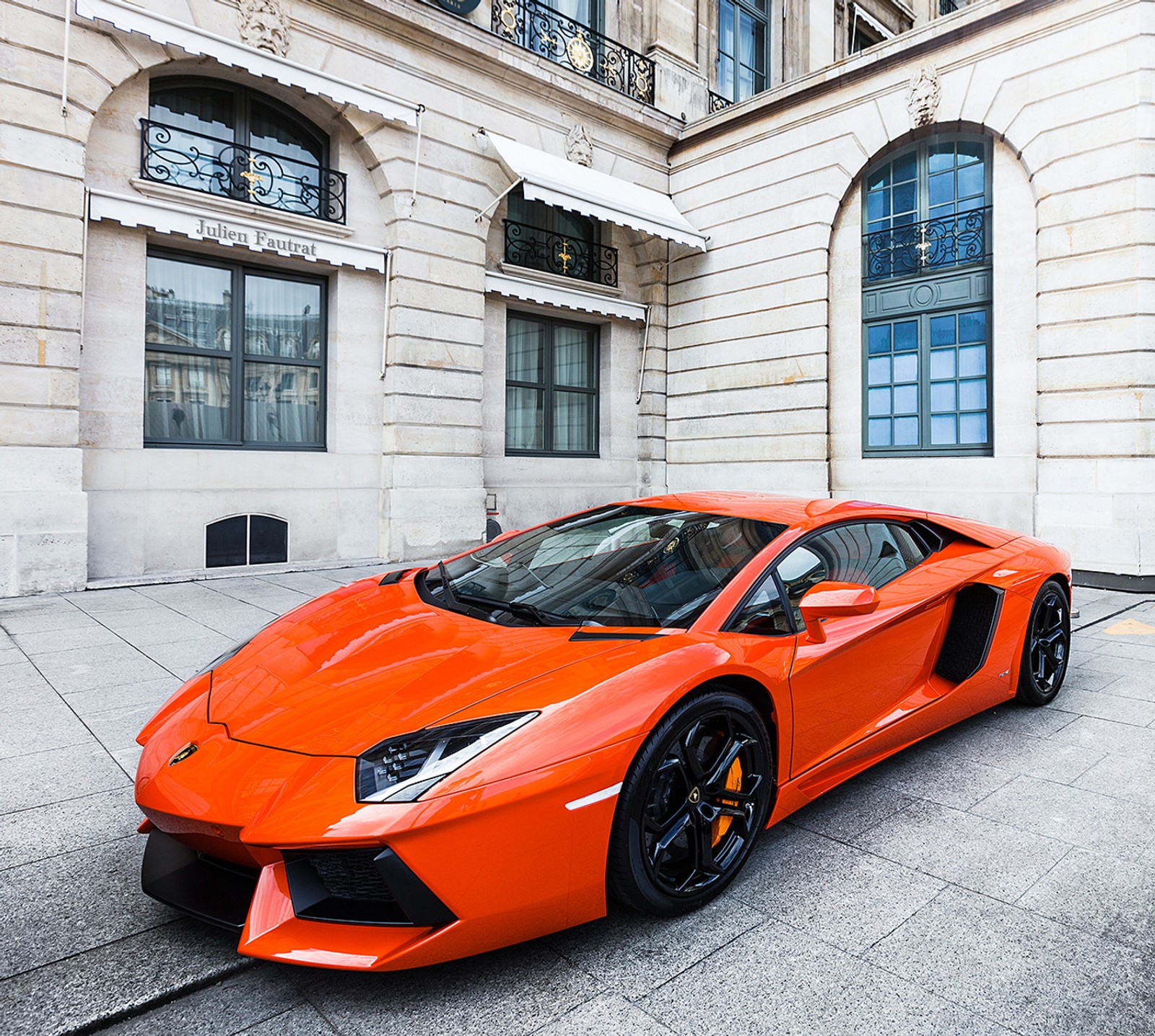 Une voiture de sport orange garée devant un grand bâtiment (auto)