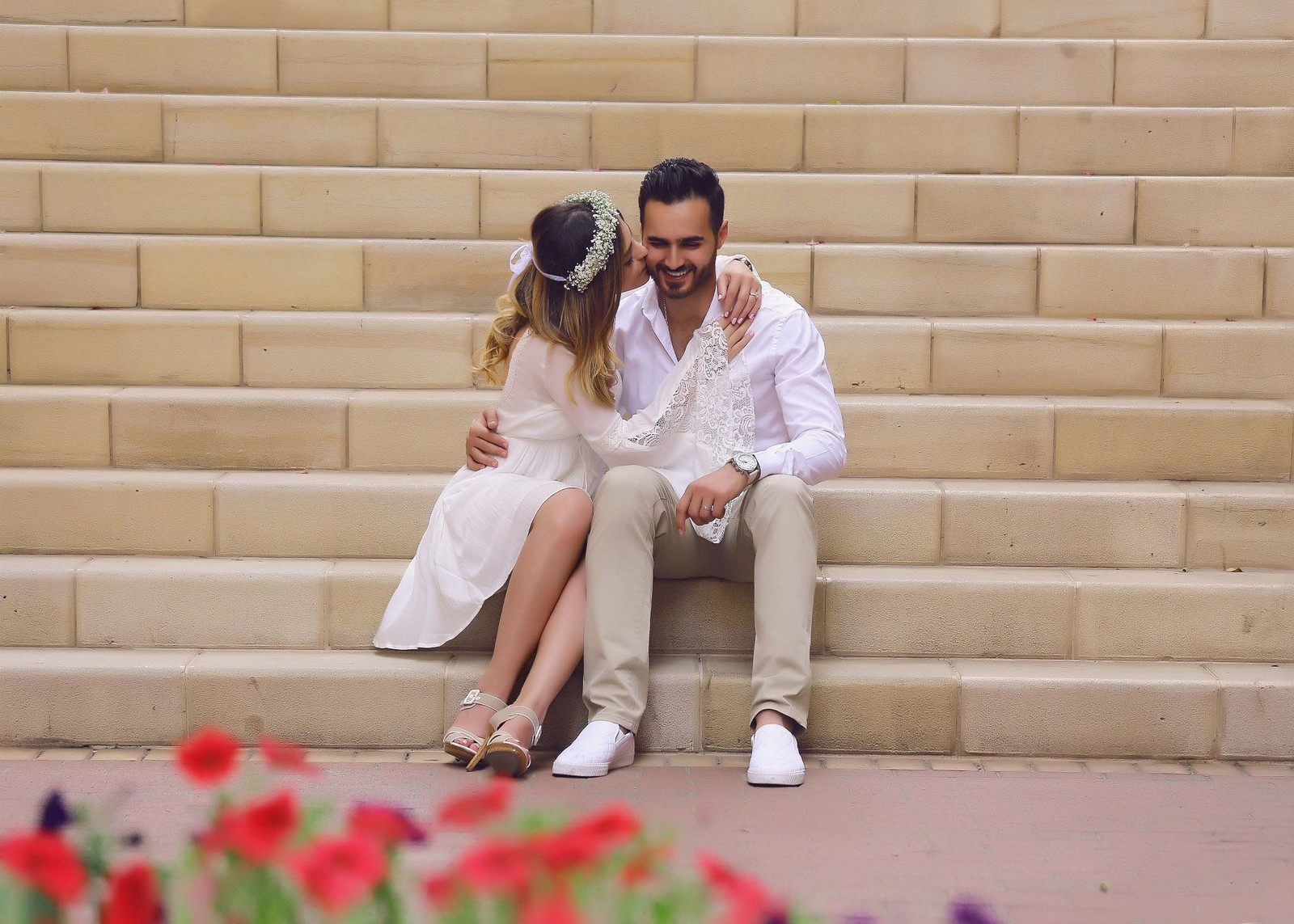 Novia y novio sentados en los escalones con flores en primer plano (pareja, beso, amor, romántico)