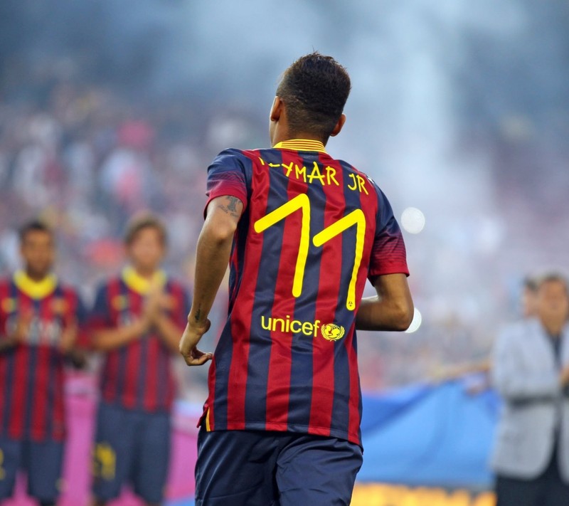 Jugador de fútbol árabe con uniforme rojo y azul de pie en un campo (jsetjh, rfhethet)