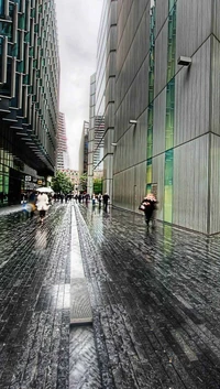 Rain-soaked city avenue with reflective pavement and pedestrians under a cloudy sky.