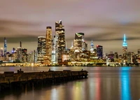 Beleuchtete Skyline von New York City bei Sonnenuntergang mit Reflexionen im Wasser