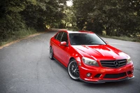 Sleek red Mercedes-Benz C-Class AMG with custom rims on a scenic road.