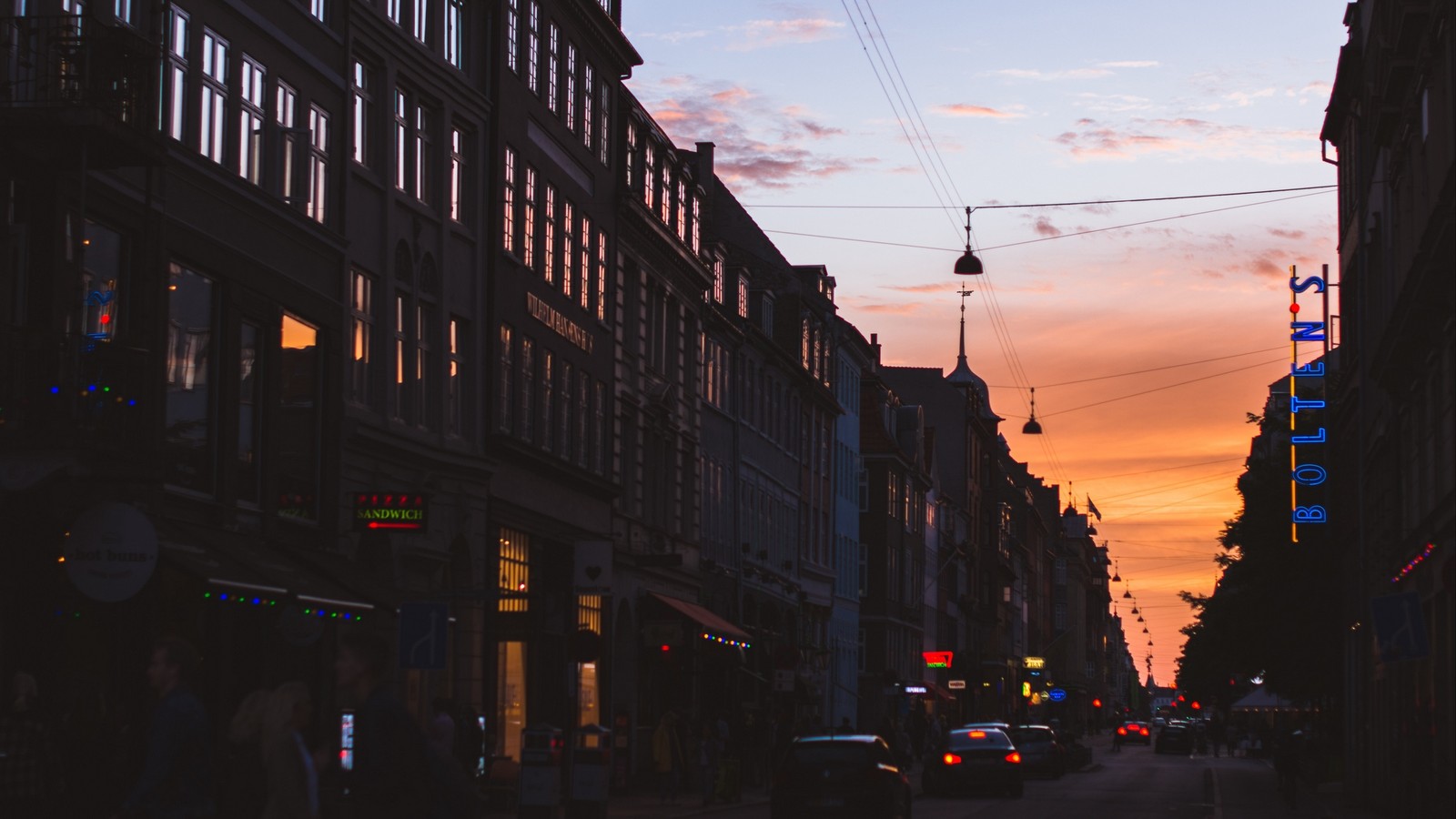 Carros estão estacionados na rua em frente a prédios ao pôr do sol (edifício, área urbana, cidade, anoitecer, rua)