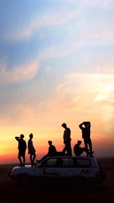 Silhouettes des membres de BTS sur un véhicule contre un ciel de coucher de soleil vibrant.