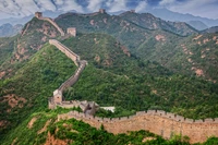 A Grande Muralha da China serpenteia por um terreno montanhoso exuberante, exibindo uma mistura de arquitetura histórica e beleza natural em meio a uma vegetação vibrante e paisagens acidentadas.