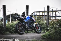 Yamaha motorcycle parked against a rustic backdrop, showcasing its sleek design amidst overgrown greenery and a cloudy sky.