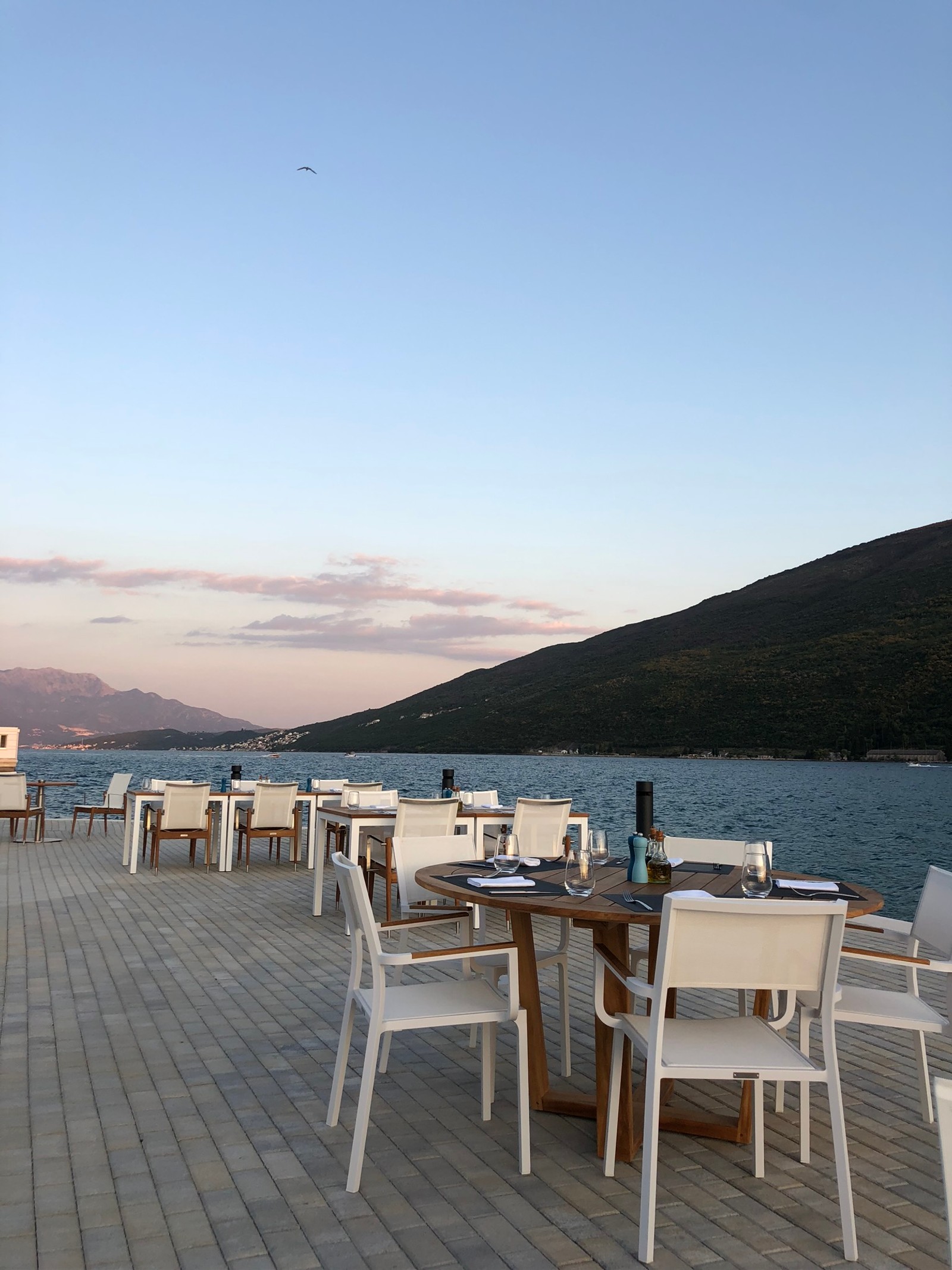 Mesas y sillas en un muelle con vista al agua y a las montañas (bienes raíces, agua, muebles, mesa, carne)