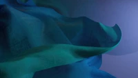 Abstract flowing fabric in shades of blue and teal, set against a soft gradient background, representing the aesthetic of Windows 11.