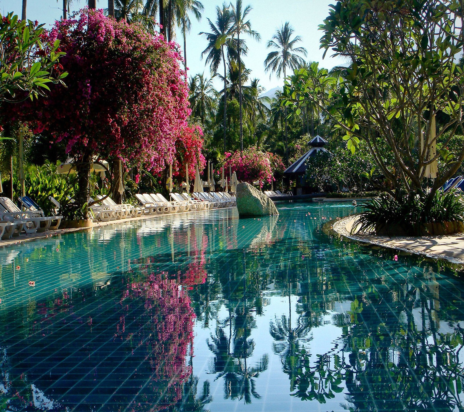 There is a pool with a waterfall and a gazebo in the background (beautiful, cute, look, nice)