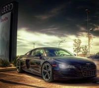 Audi R8 garé sous un panneau Audi contre un ciel dramatique.