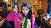 IU dans une tenue vibrante montre son style dynamique et son charisme dans un cadre coloré.