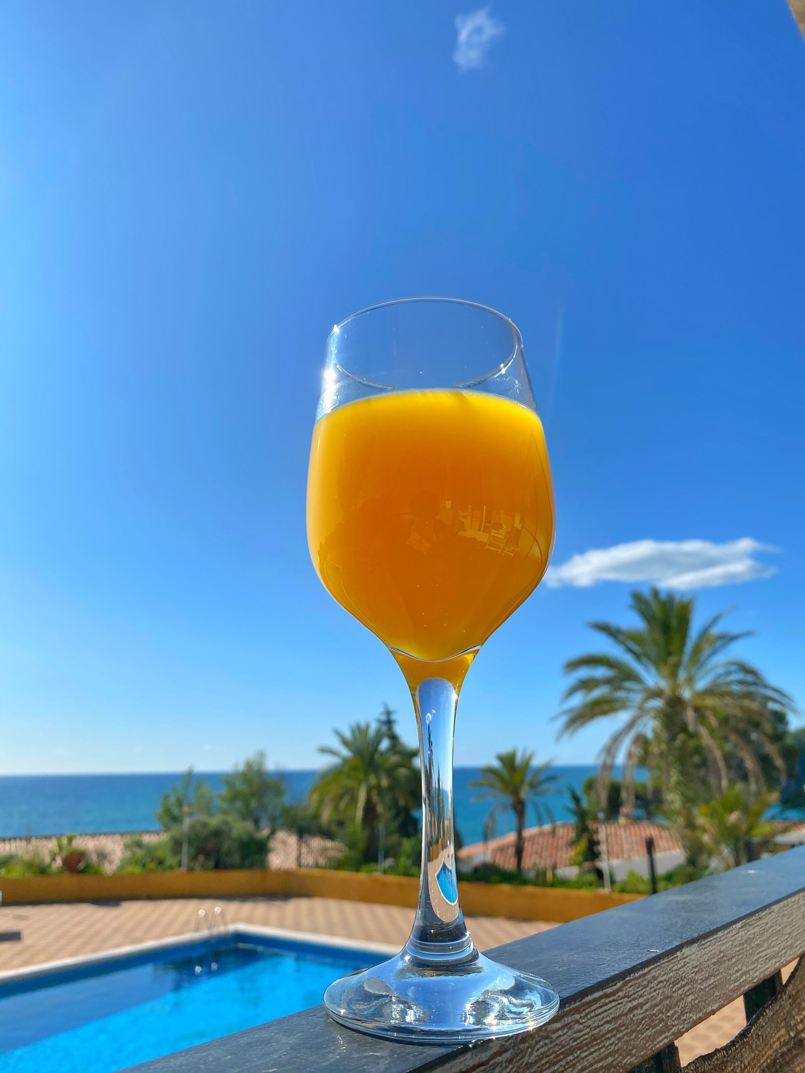 There is a glass of orange juice on a table by the pool (drink, wine, juice, wine glass, liquid)