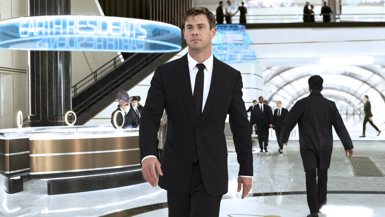 Imagen de un hombre en traje y corbata caminando por un vestíbulo (hombres de negro internacional, película, chris hemsworth)