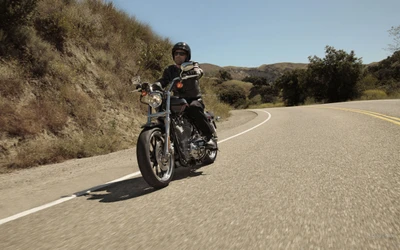 Rider on a custom Harley Davidson Sportster cruising along a winding asphalt road.