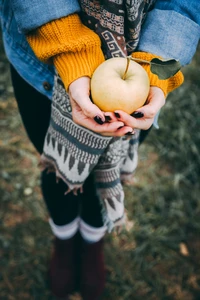 Kind hält einen gelben Apfel im herbstlichen Gras