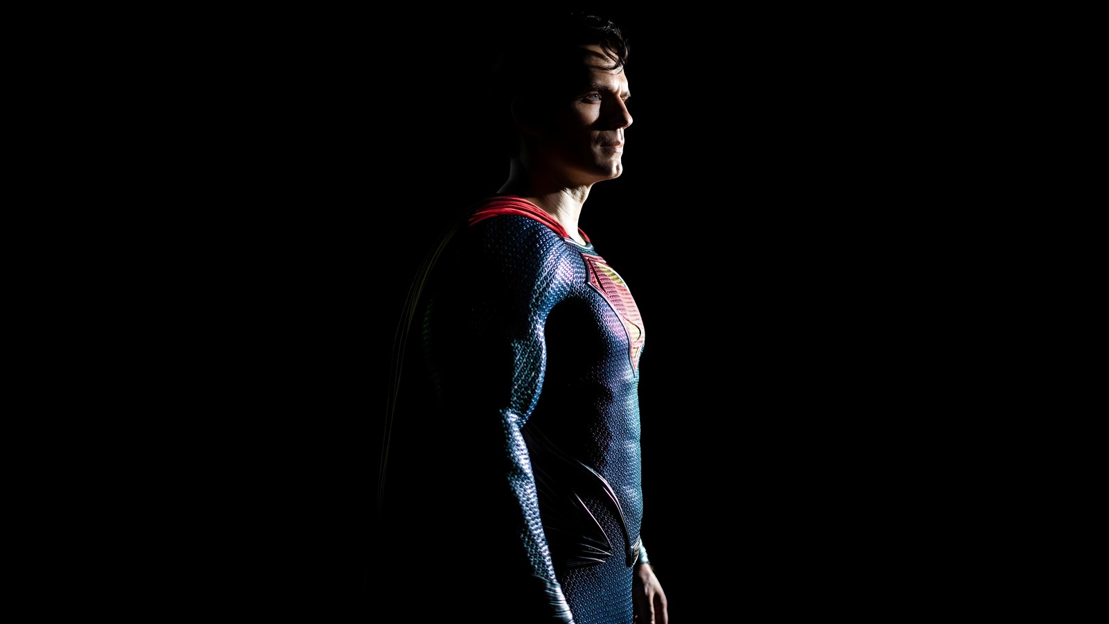 Un primer plano de un hombre en un traje de superman de pie en la oscuridad (superman, superhéroes de dc, dc superheroes, henry cavill, dc comics)