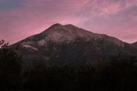 Majestic mountain ridge at dusk under a vibrant pink sky.