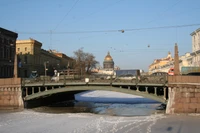 Bogenbrücke über gefrorenem Wasserweg mit historischen Gebäuden und der Isaakskathedrale in Sankt Petersburg