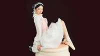 Joy de Red Velvet dans une robe fantaisiste, assise élégamment sur un gâteau, incarnant le thème enchanteur de "Ressens mon rythme".