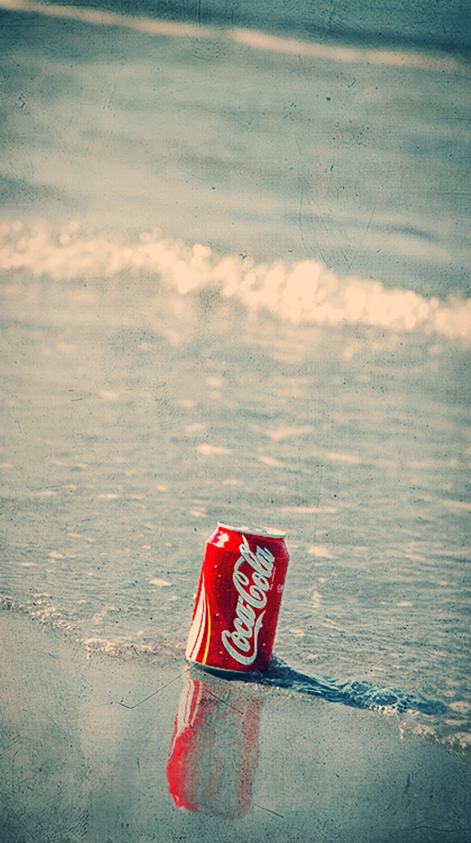 Une canette de coca-cola arabe posée sur la plage dans l'eau (plage, coca cola, moment, été)