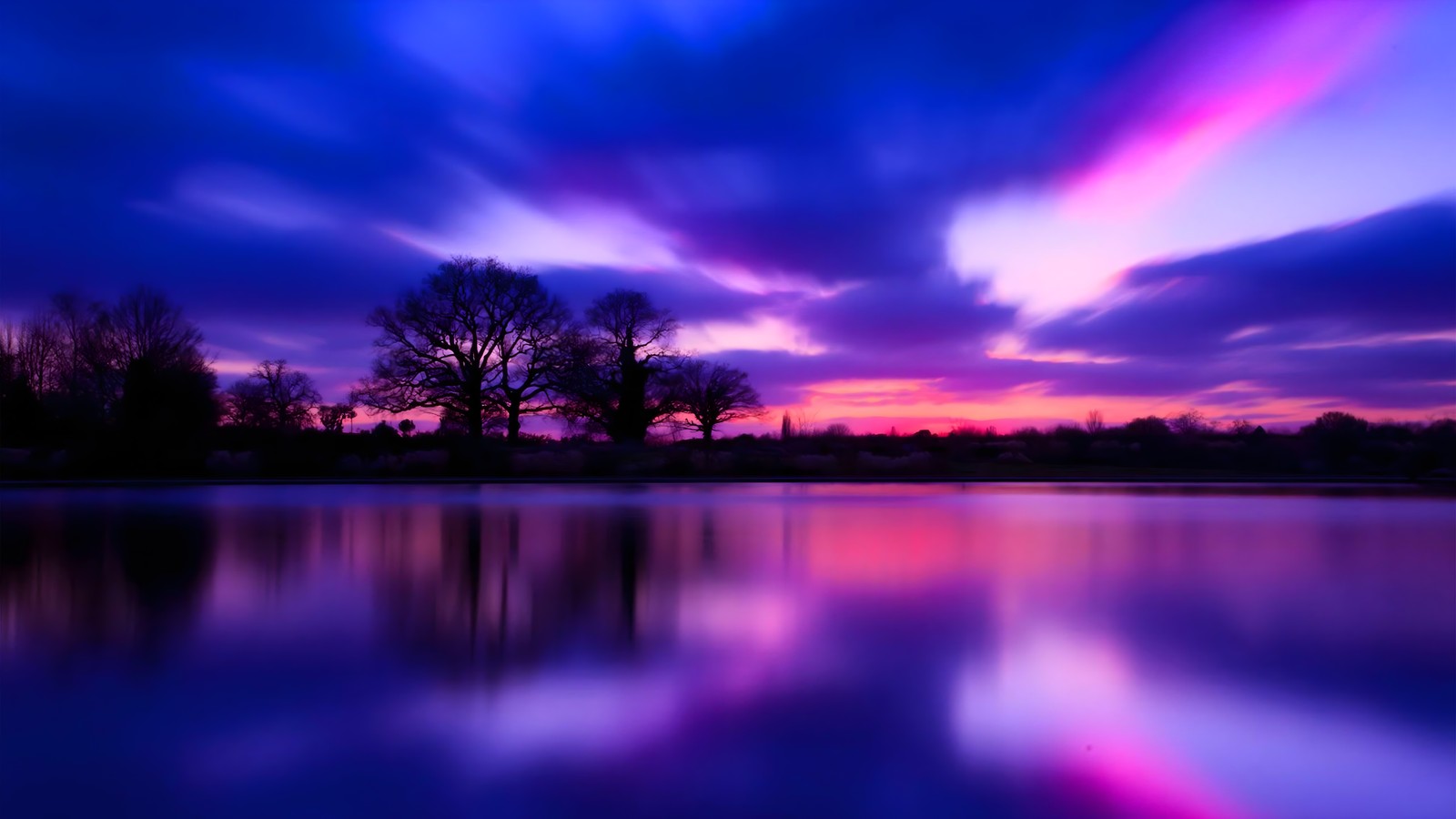 Un coucher de soleil violet et bleu sur un lac avec des arbres (coucher de soleil, bleu, nuage, eau, ressources en eau)