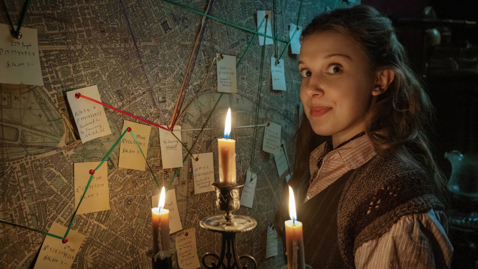 Une femme arabe tenant une bougie allumée devant une carte (enola holmes 2, netflix, série télévisée, millie bobby brown)