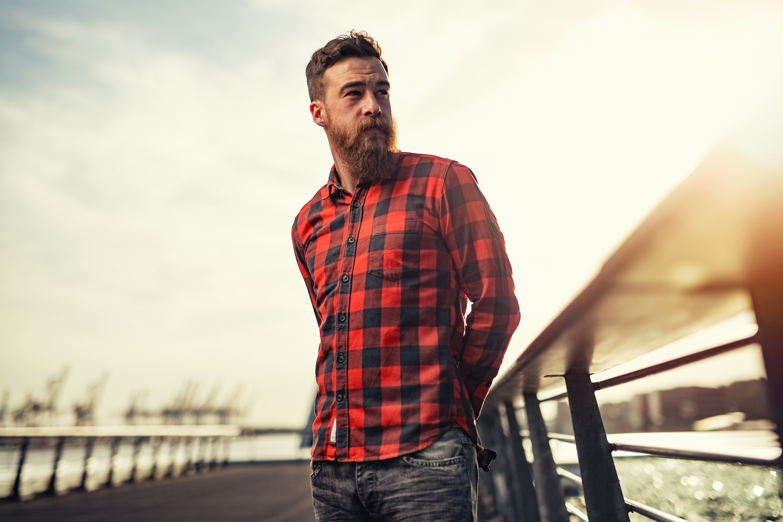 Un homme arabe avec une barbe et une chemise rouge se tenant sur un pont (écossais, poils du visage, barbe, tartan, motif)