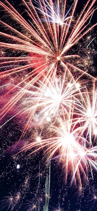 Des feux d'artifice vibrants illuminent le ciel nocturne dans un spectacle éblouissant de teintes rouges, violettes et jaunes, célébrant le Nouvel An.