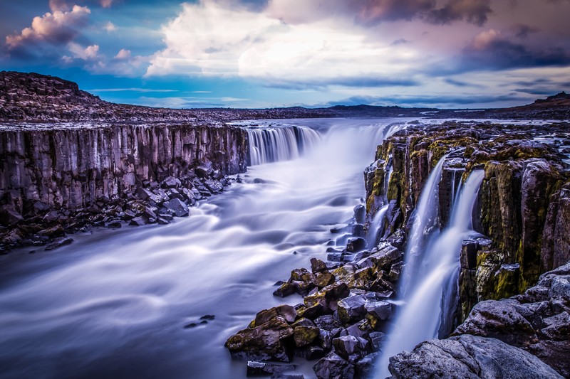 Водопад, стекающий по камням в реку под облачным небом (selfoss waterfall, исландия, пейзаж, река поток, длительная выдержка)