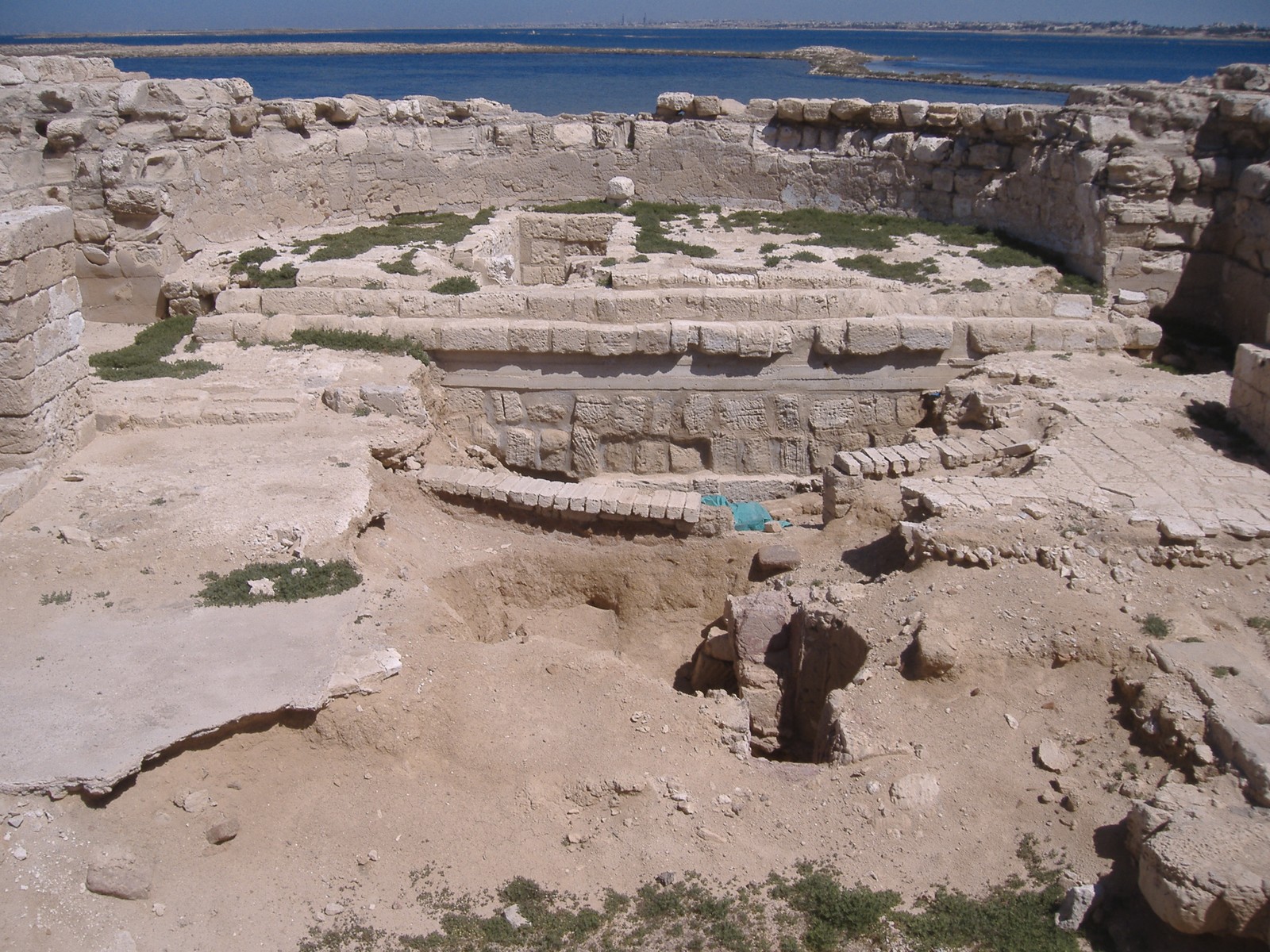 Arafed stone structure in a desert area with a body of water in the background (archaeological site, archaeology, ancient history, history, historic site)