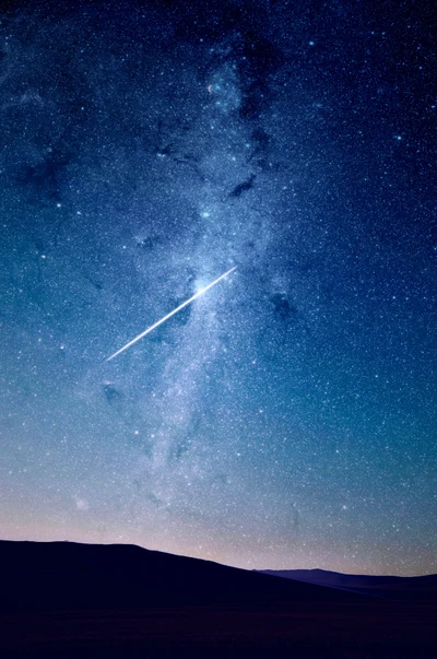 Una vista impresionante de la galaxia Vía Láctea iluminada contra un profundo cielo nocturno azul, con una estrella fugaz atravesando un mar de estrellas sobre un paisaje silueteado.