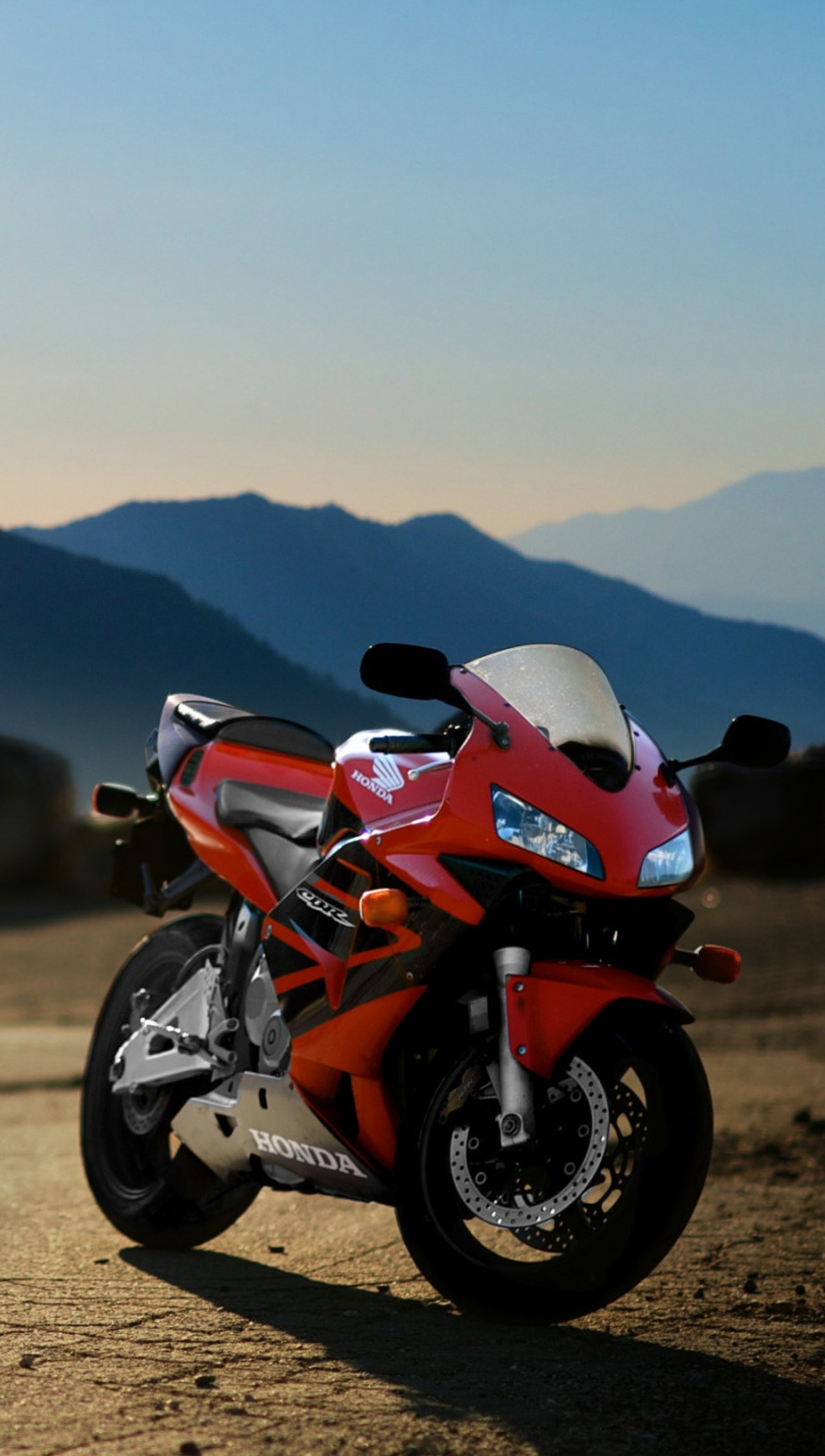 Hay una motocicleta roja estacionada en un campo con montañas al fondo (bicicleta, honda, rojo)