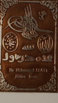 Inscripción de caligrafía islámica y el nombre del Profeta Muhammad (la paz sea con él) en una placa decorativa.