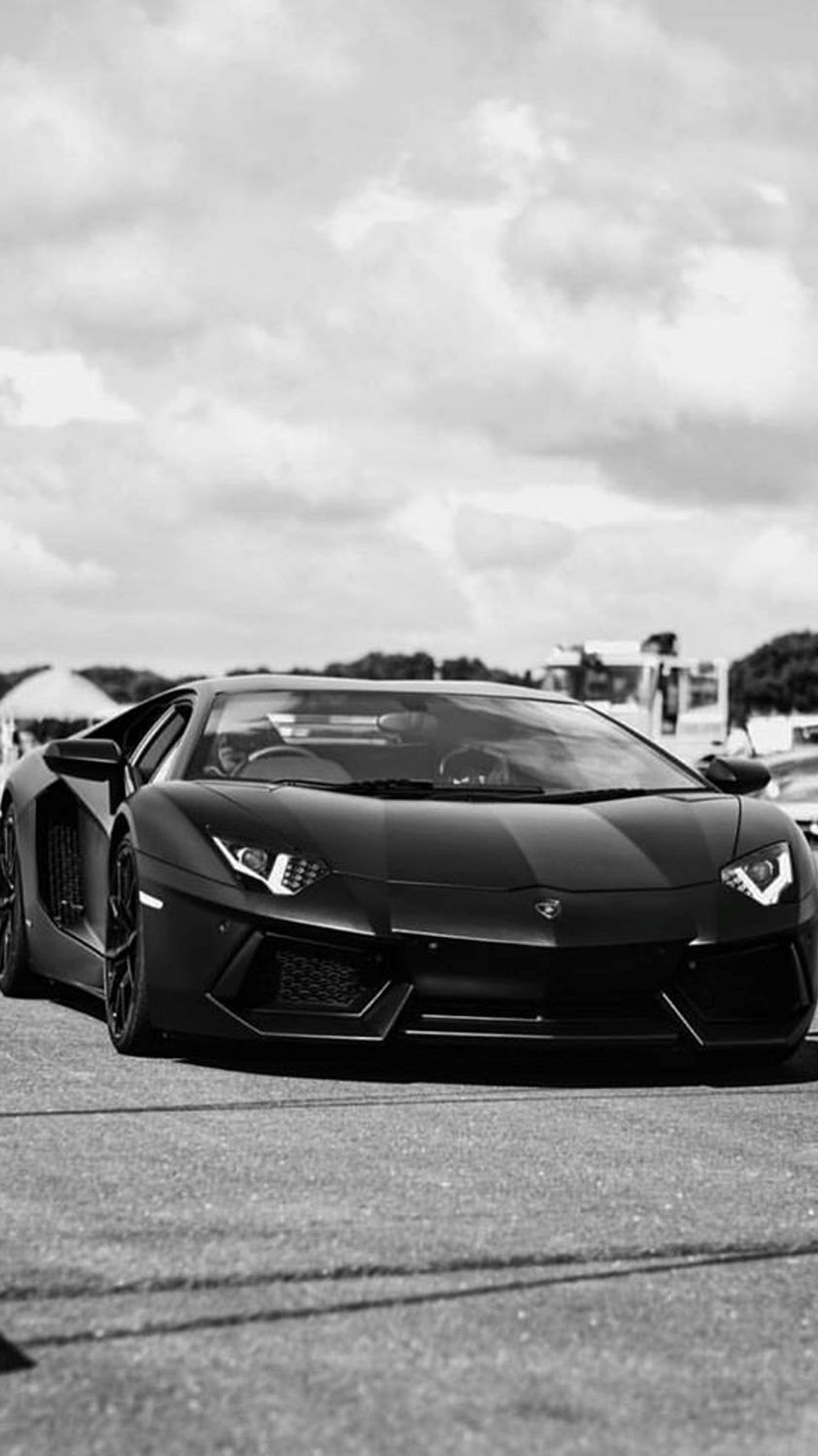 Una foto en blanco y negro de un lambo estacionado en un aparcamiento (negro, coche, lamborghini)