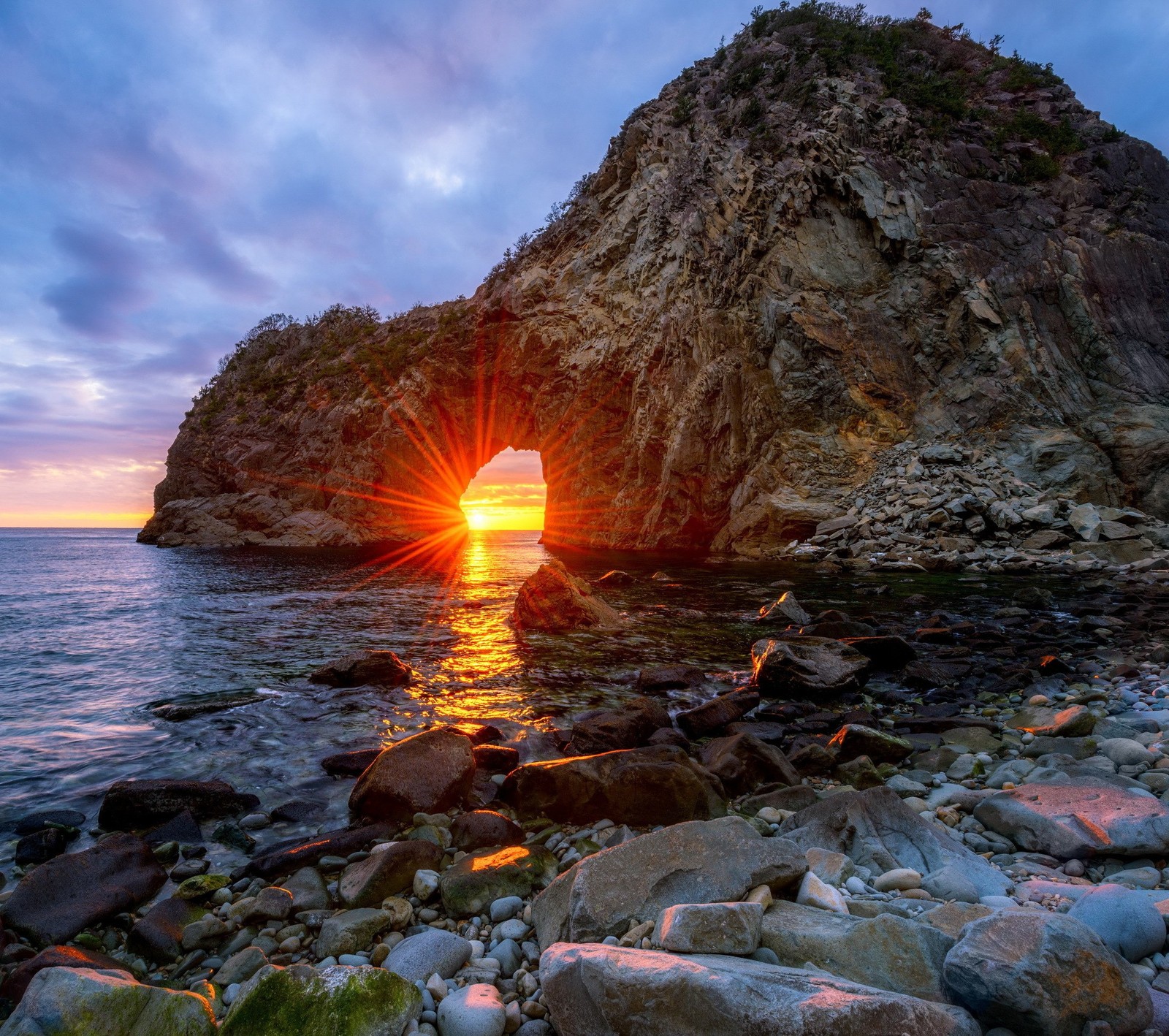 A view of a rock formation with a sun setting in the background (beach, japan, rock, sea, sunset)